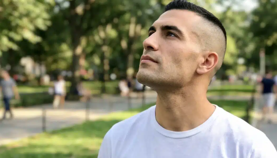Close-up of a man with a high fade and short dark hair looking upward in a green park setting