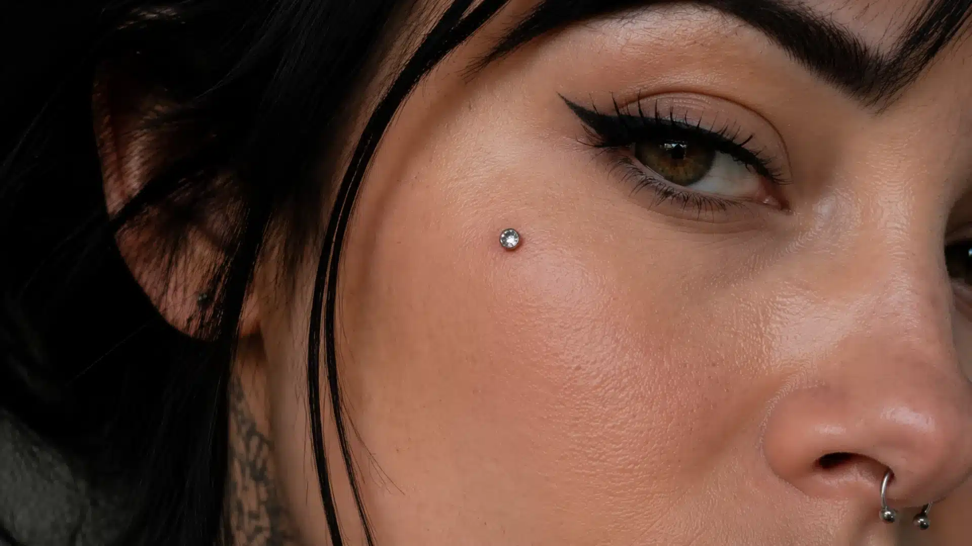 Close-up of a woman’s cheek with a flat crystal dermal piercing near her eye