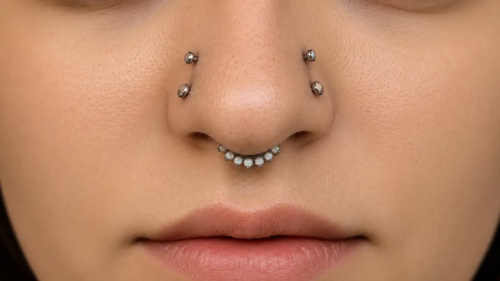 Close-up of a nose with four symmetrical nostril studs and an opal septum clicker ring in