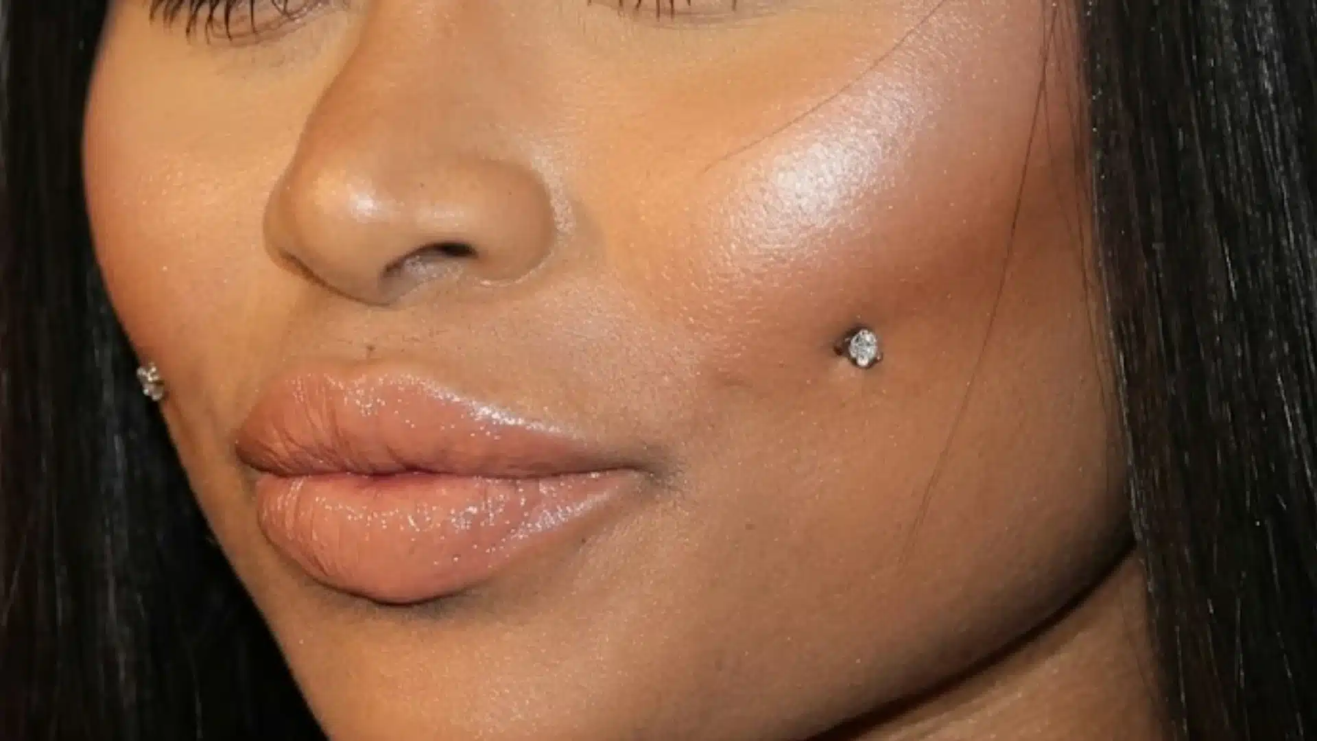 Close-up of a person's lower face featuring glossy lips and cheek dimple piercings