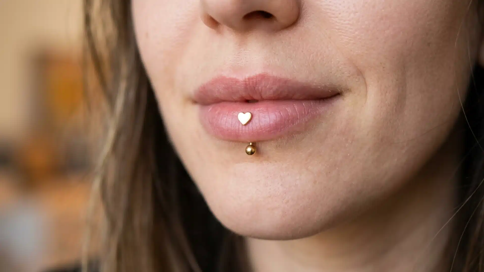 Close-up of a person's lower lip with a gold vertical labret piercing featuring a heart-shaped top stud