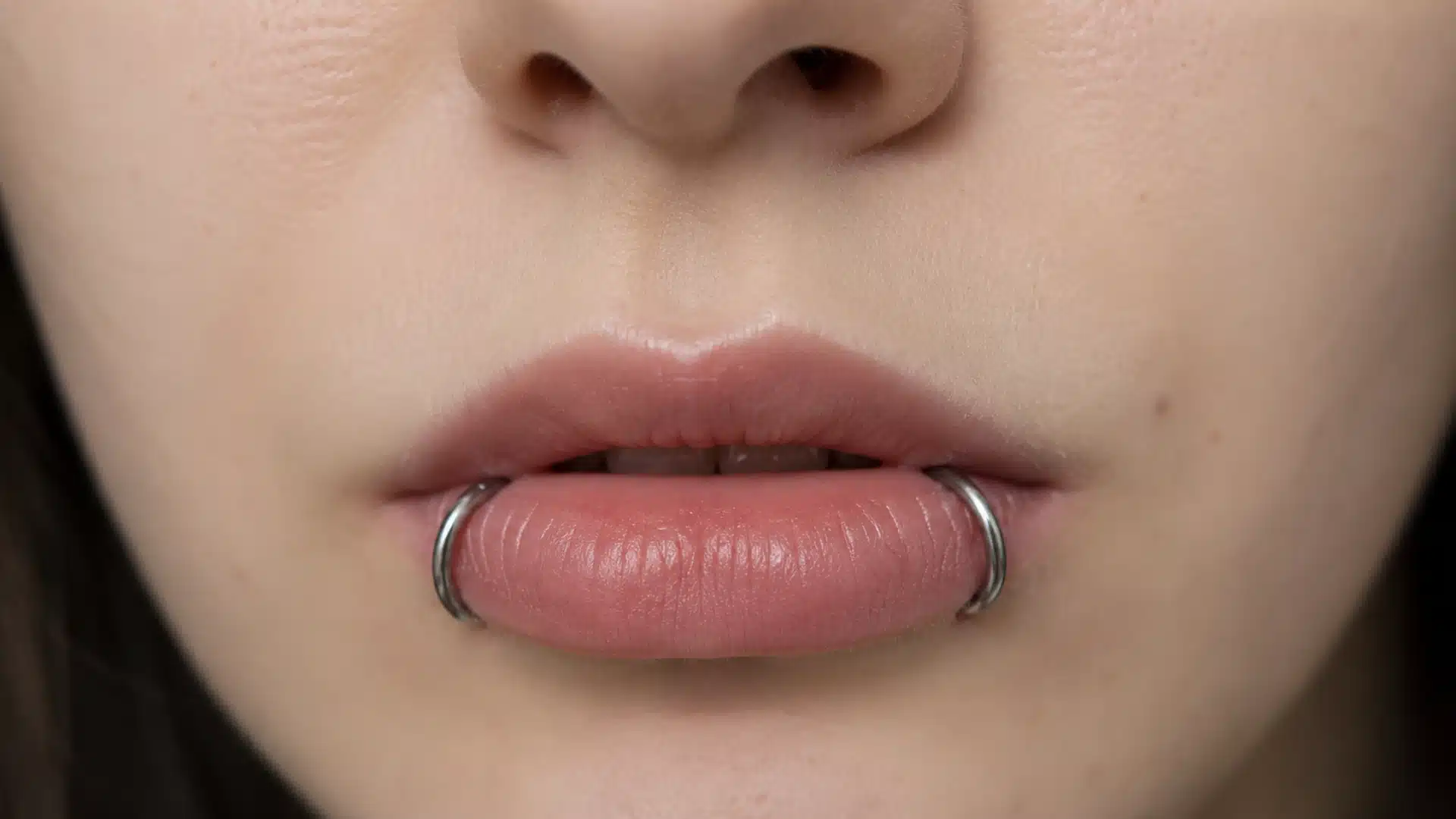 Close-up of a person's slightly parted lips featuring a silver snake bites piercing with two rings