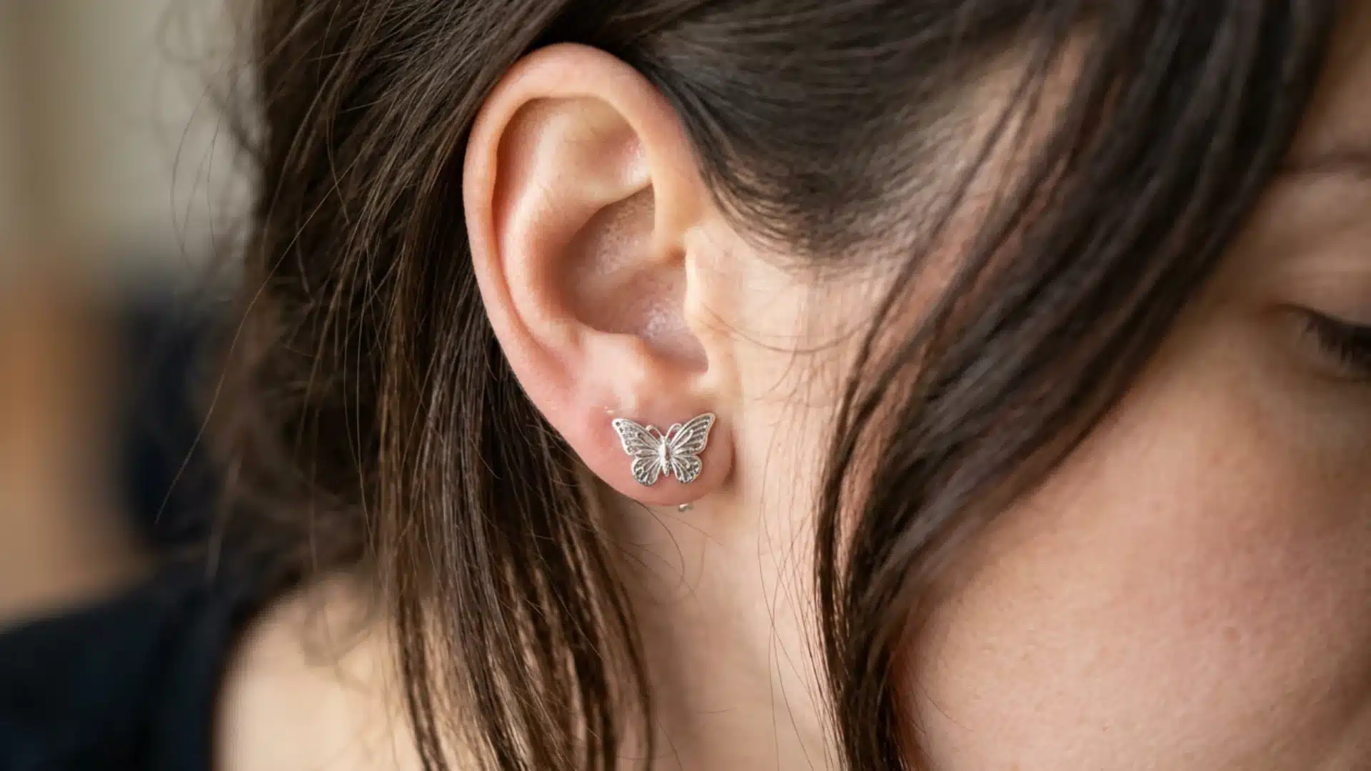 Close-up of a woman with dark hair, showing her ear adorned with a detailed silver butterfly stud earring