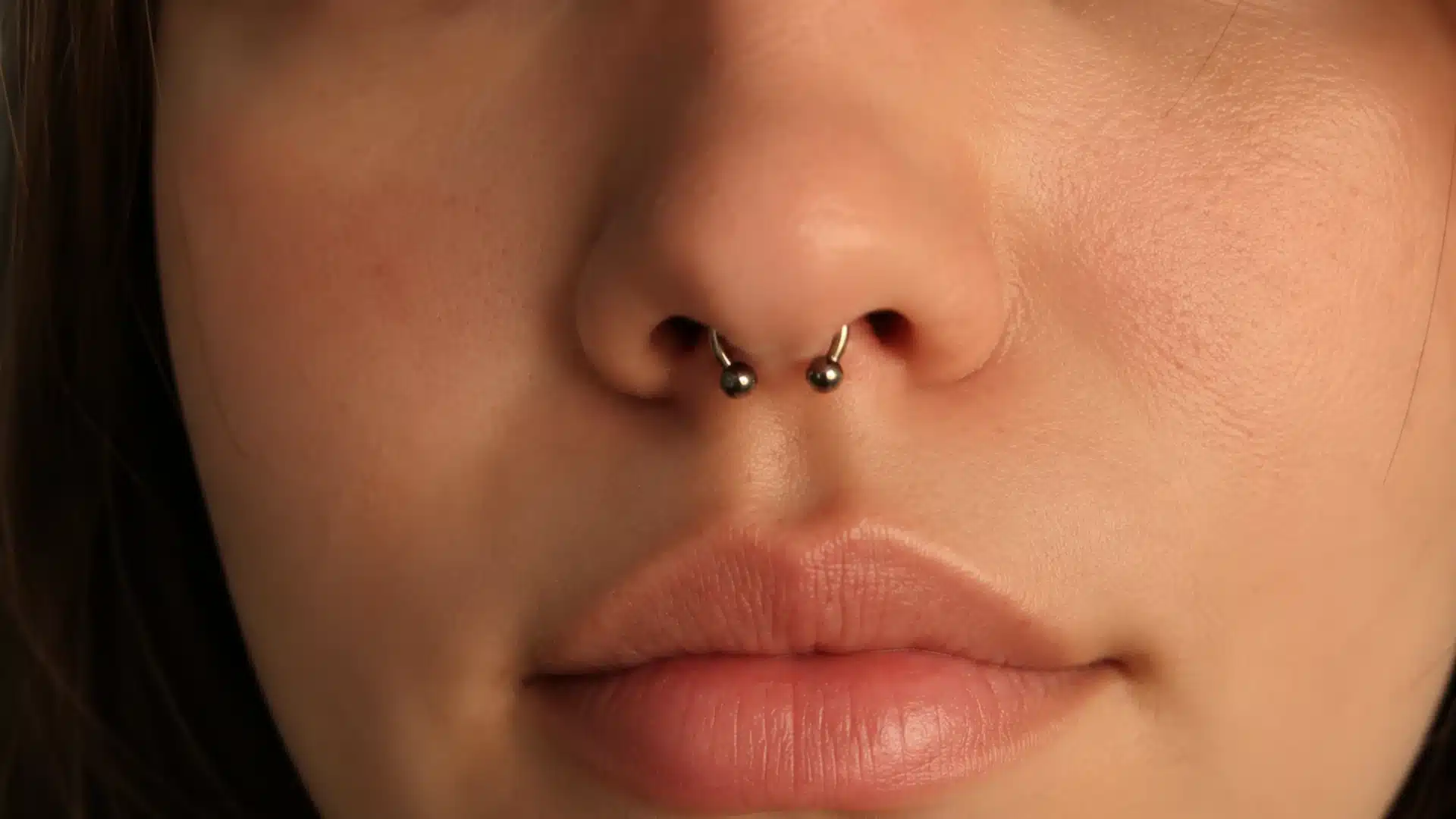 Close-up of showing a person's nose and lips, featuring a metallic circular barbell septum piercing