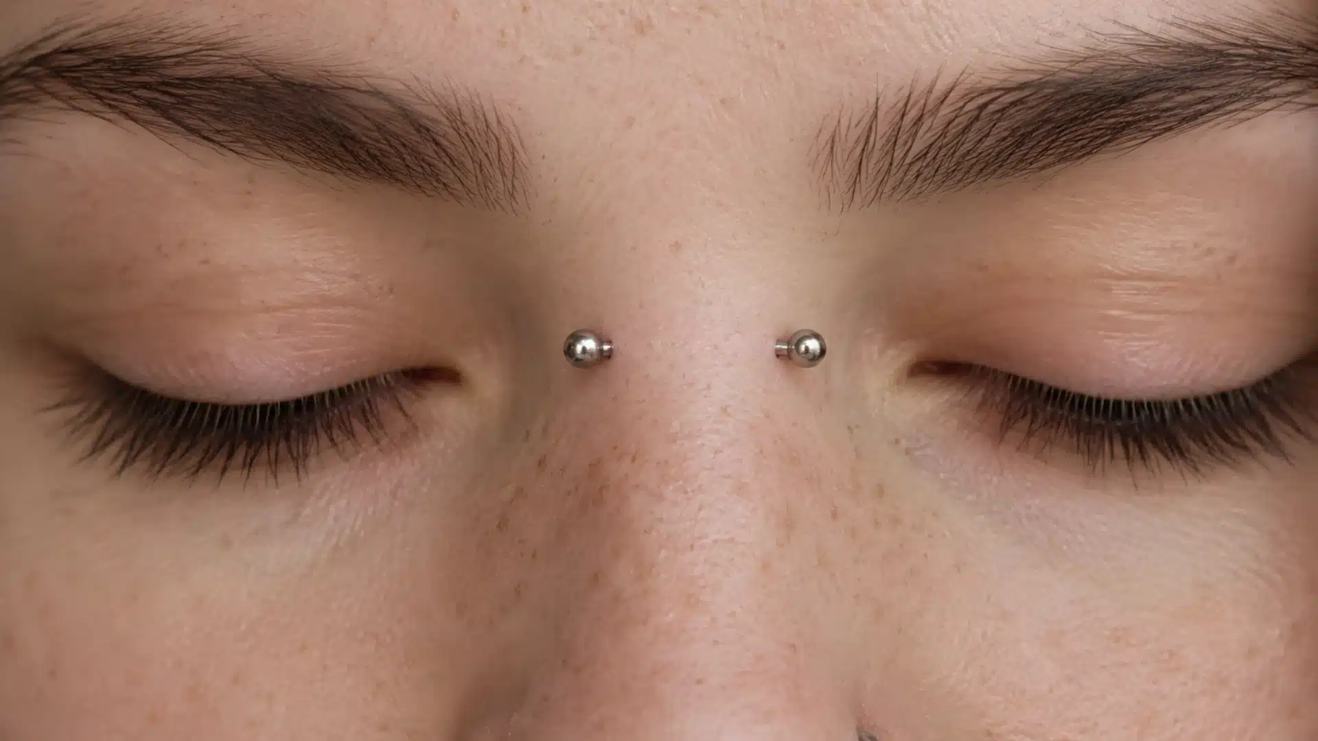 Close-up of showing a person with closed eyes and a silver bridge piercing on their nose