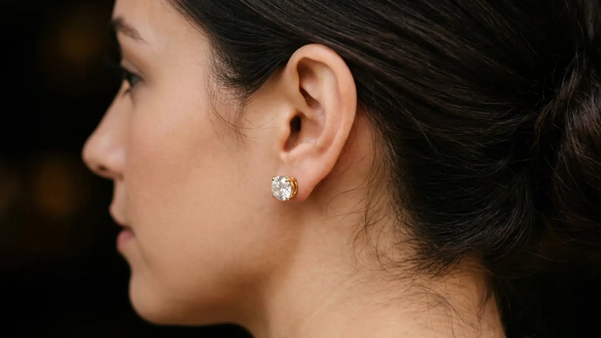 Close-up profile of a woman with her hair tied up, wearing a large round diamond stud earring set in gold