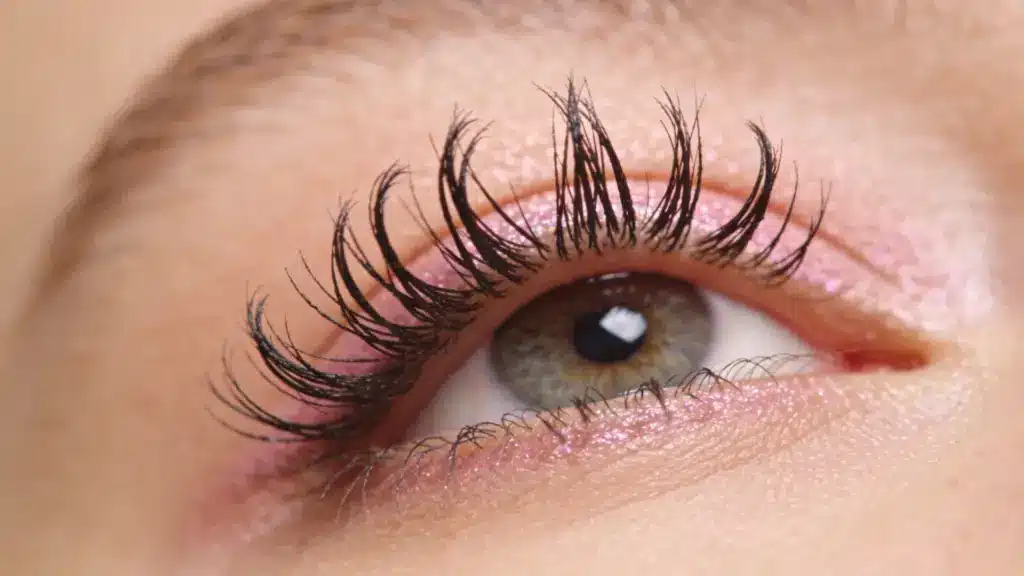 Closeup of a green eye with long curled black lashes and shimmering pink eyeshadow