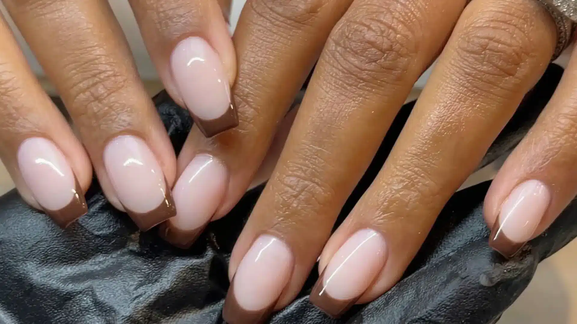 Close up of chocolate brown French tips on short square nails with nude base and glossy finish