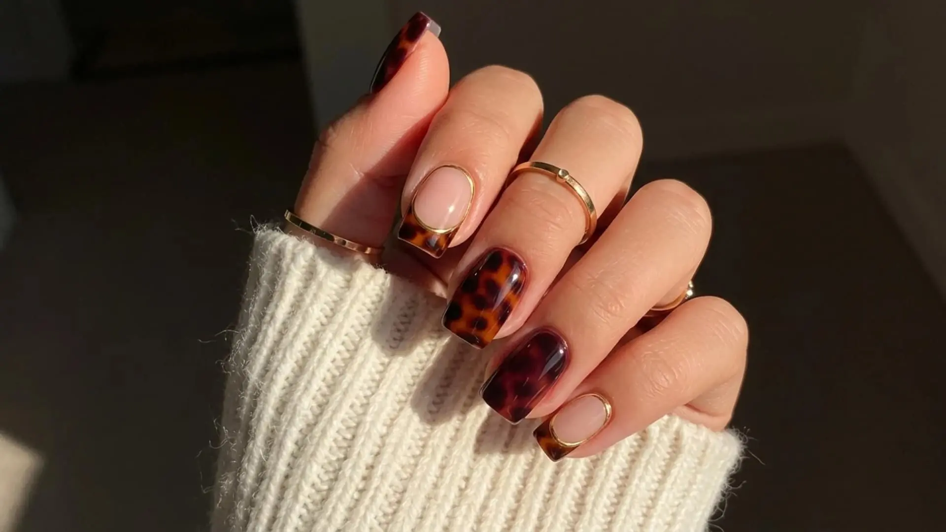 Close up of square nails with tortoiseshell pattern and nude base with gold outline accents