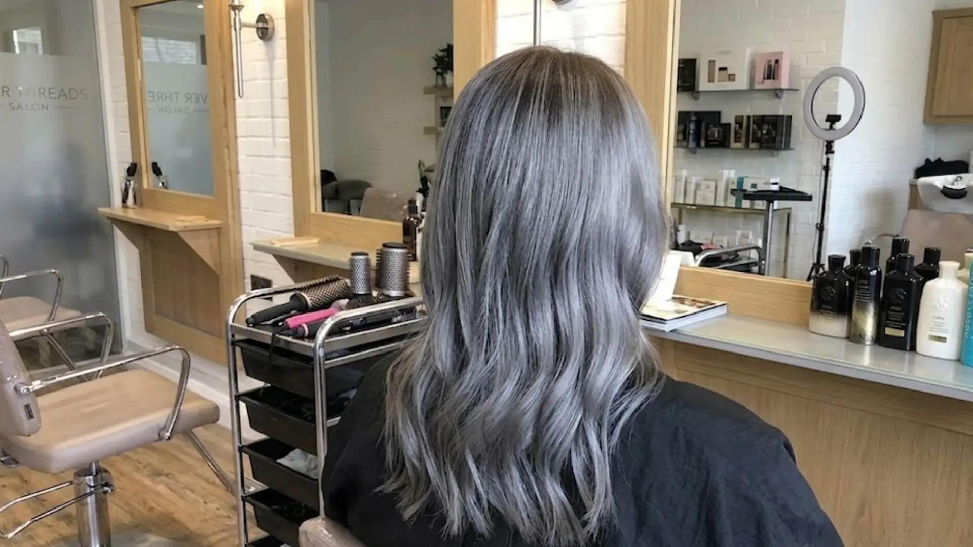 Cool toned charcoal gray hair styled in soft waves at salon, showing smooth finish and even color