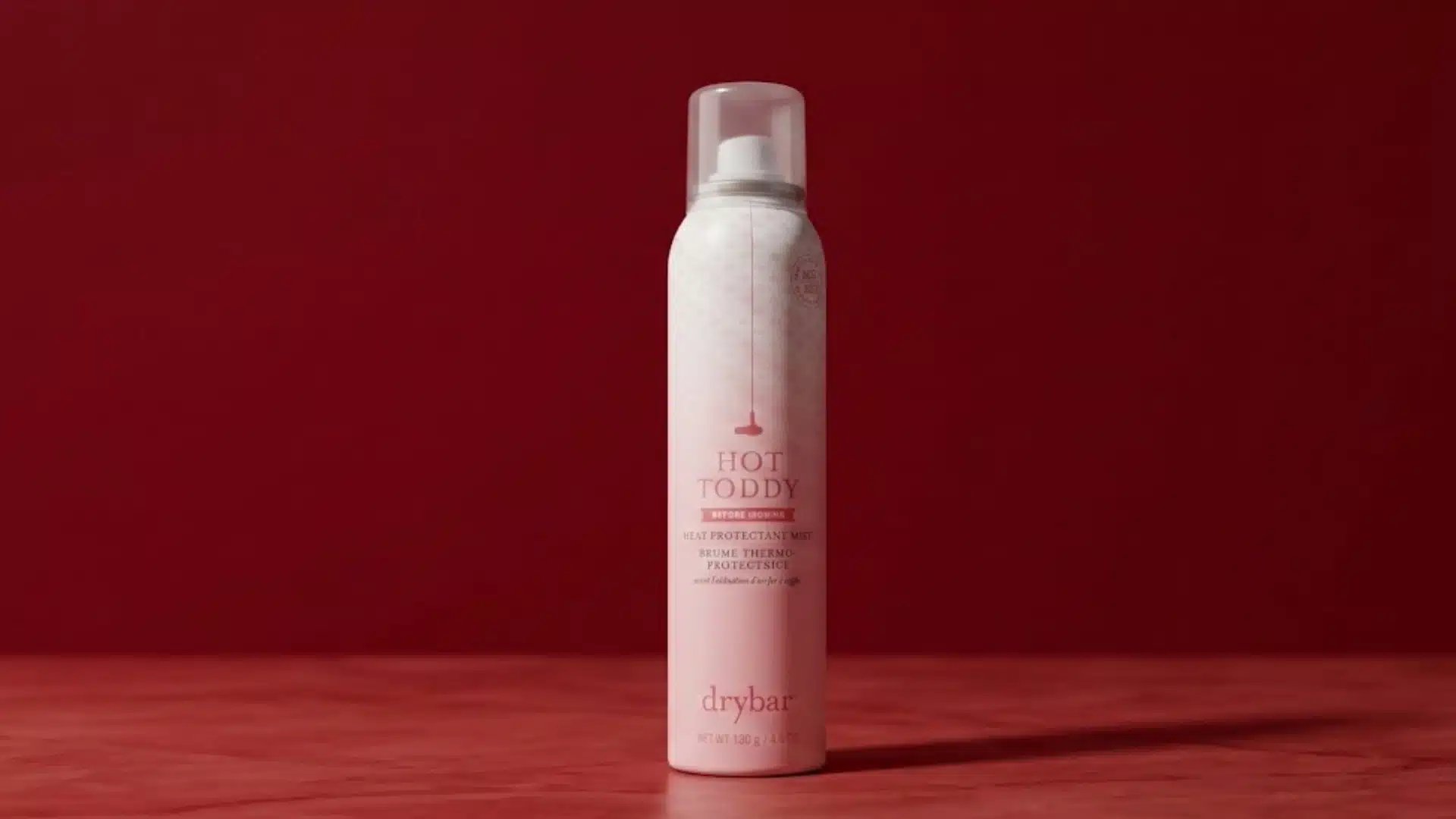 Drybar Hot Toddy heat protectant mist spray can on a red background with warm studio lighting