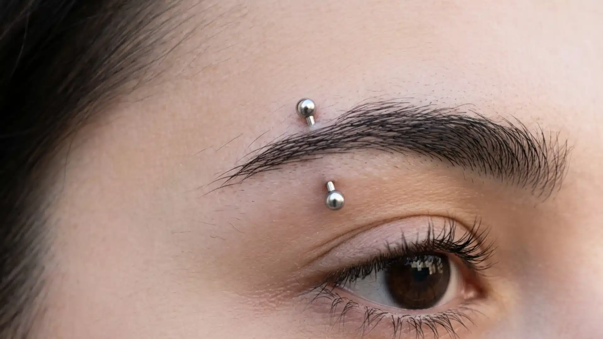 Extreme close-up of a person's eye and eyebrow featuring a silver curved barbell eyebrow piercing