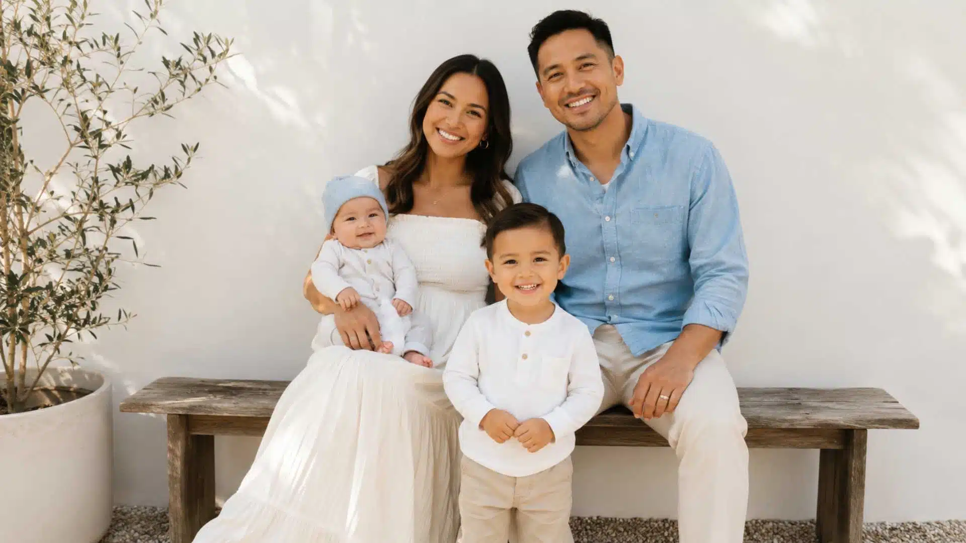 Family in ivory, blue, and cream coordinated newborn session outfits on outdoor wooden bench