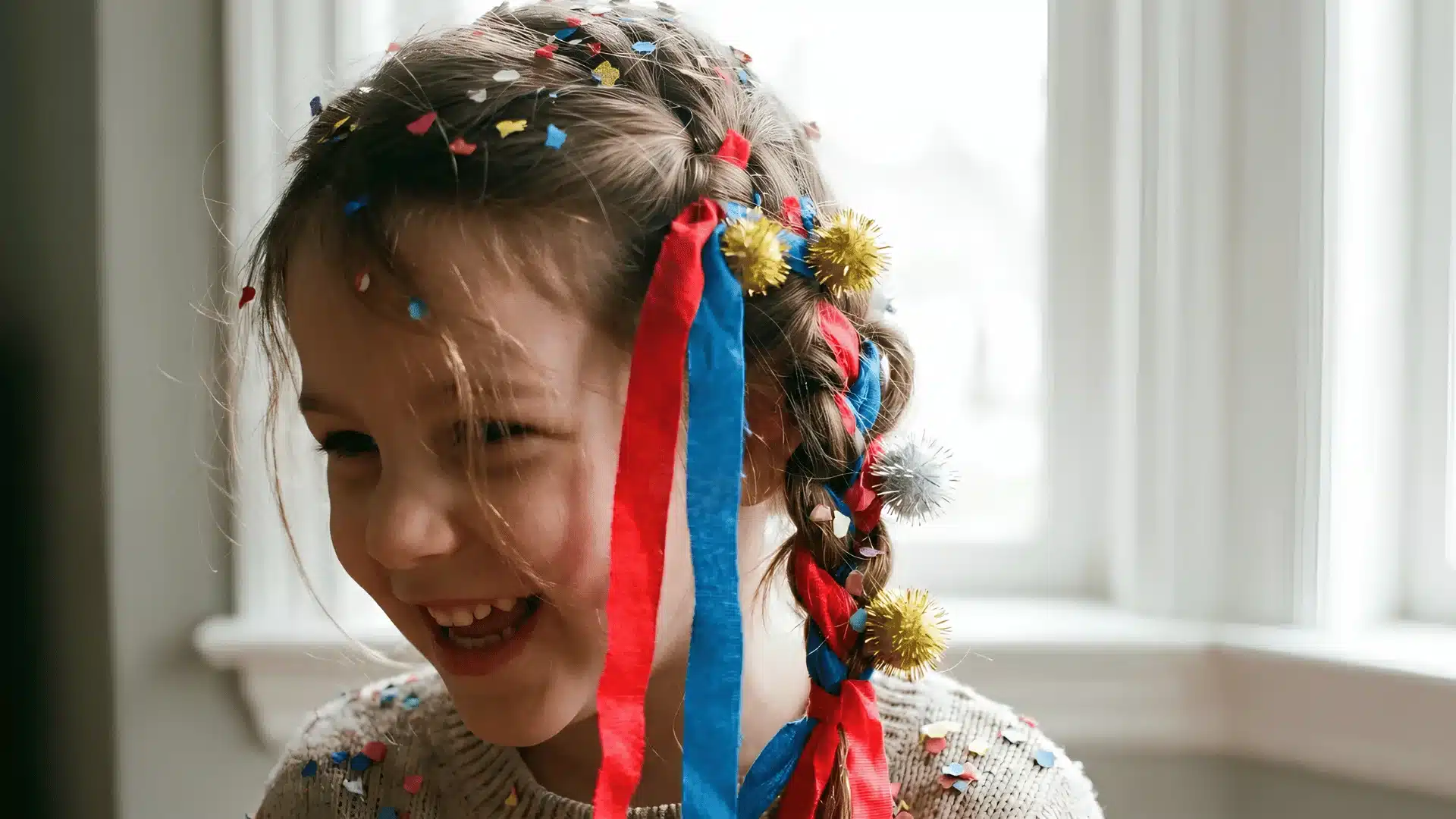 Girl with braided hair, ribbons, and confetti laughing by window