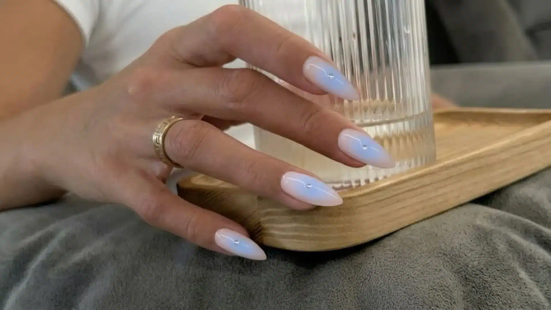 Glossy pastel blue ombre almond nails holding glass, minimal elegant manicure with soft gradient finish