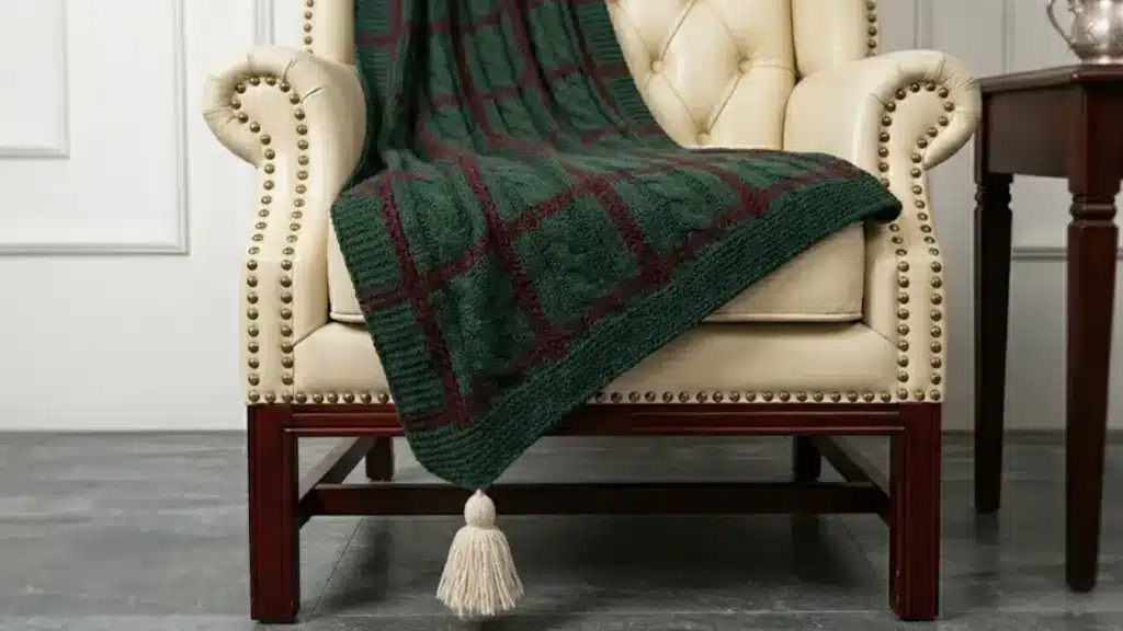 Green knitted acrylic throw blanket with burgundy plaid pattern draped over a cream armchair