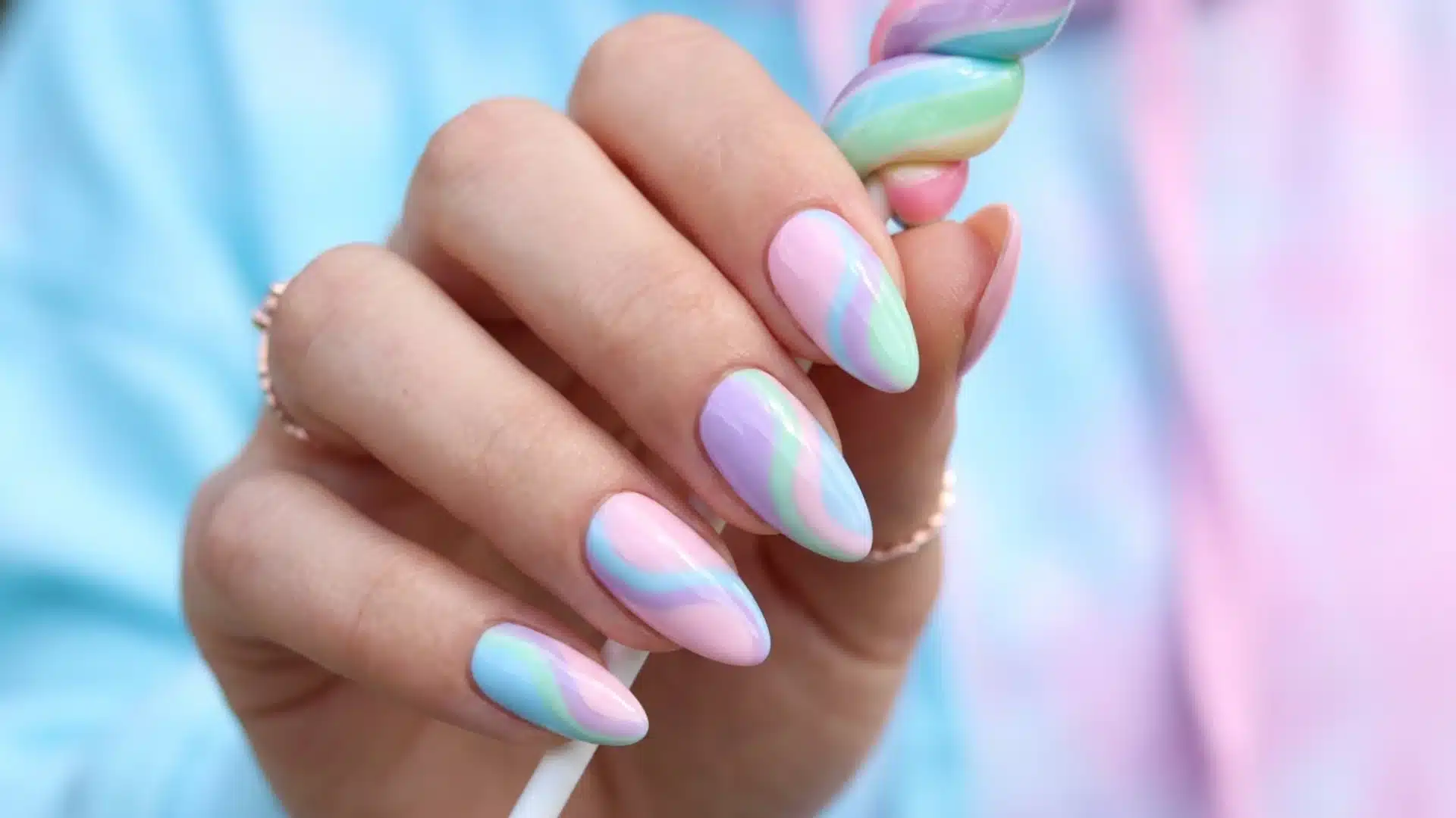 Hand with almond Candy Swirl nails in pastel pink, blue, and green waves, glossy finish, soft playful spring nail design
