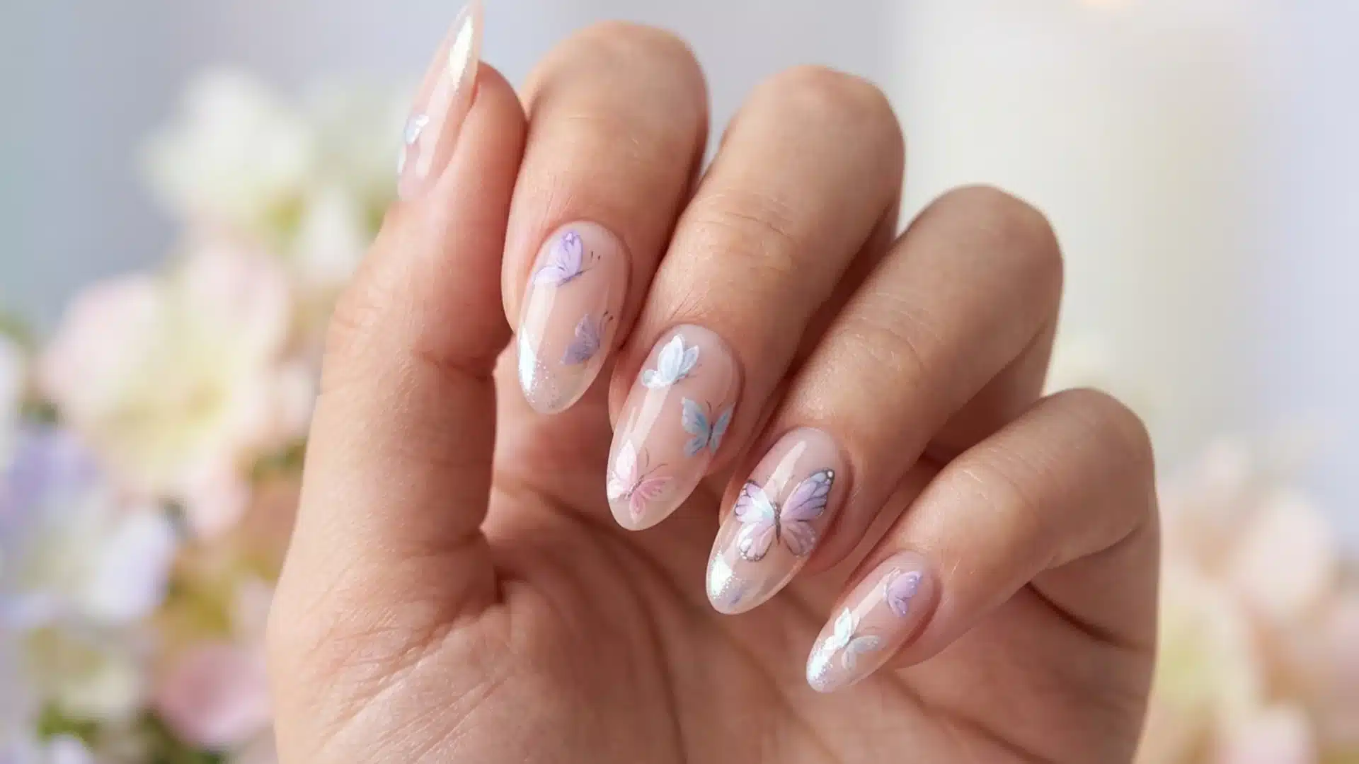 Hand with almond nails featuring soft butterfly nail art, pastel tones with glossy finish