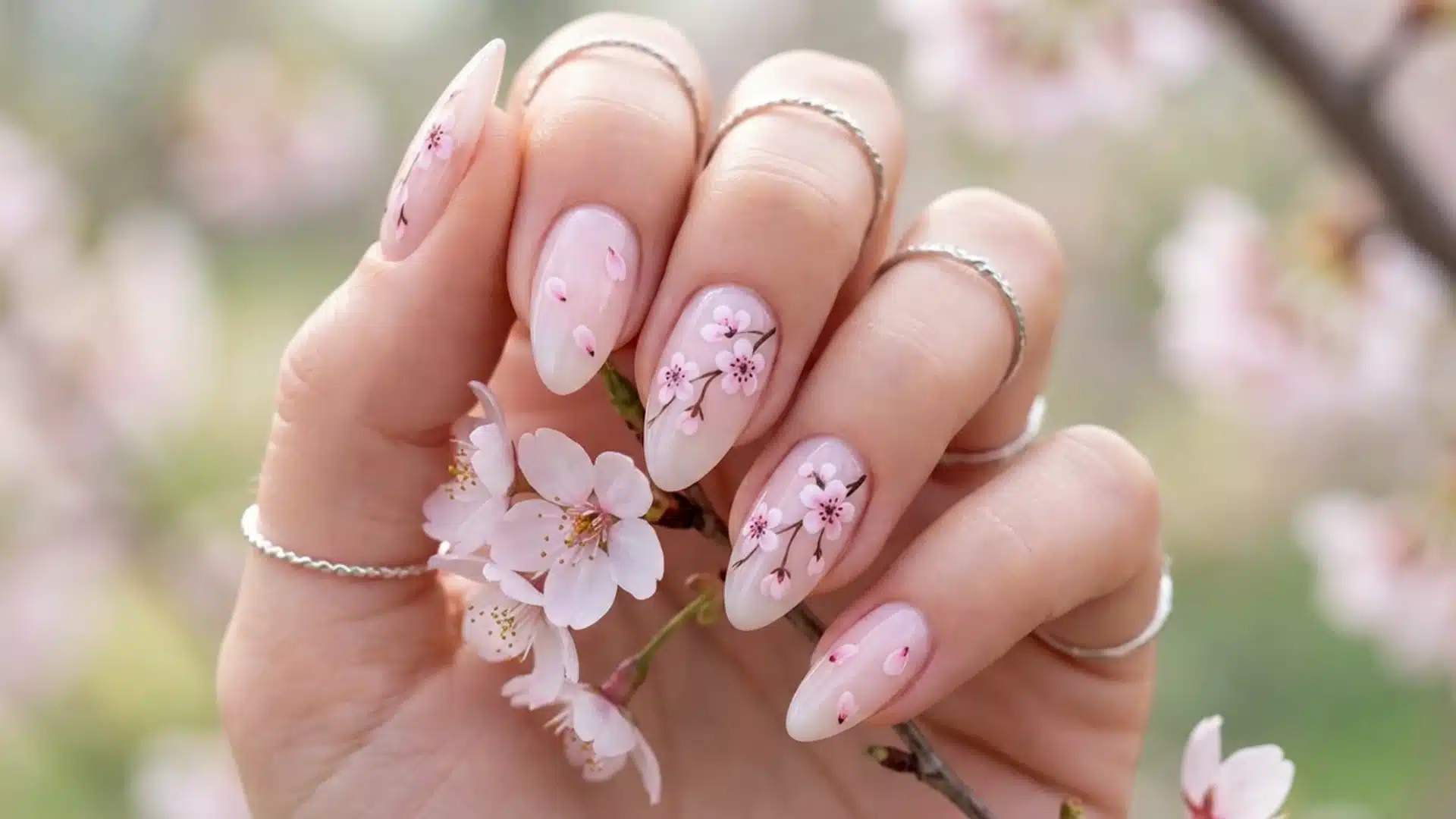 Hand with almond nails featuring soft pink cherry blossom nail art, delicate floral design, glossy finish