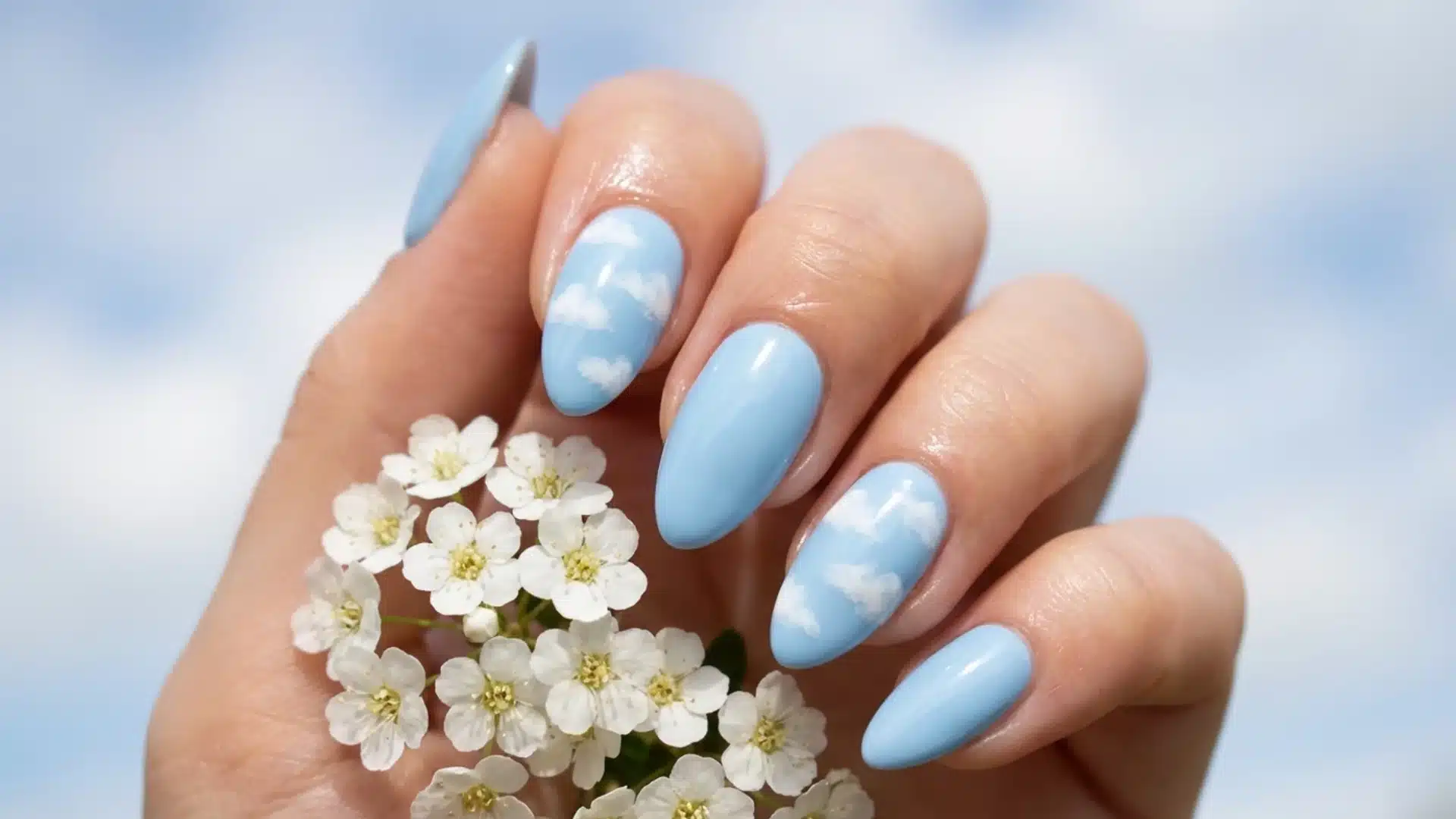 Hand with almond nails in soft baby blue with cloud nail art, glossy finish, calm sky-inspired spring design