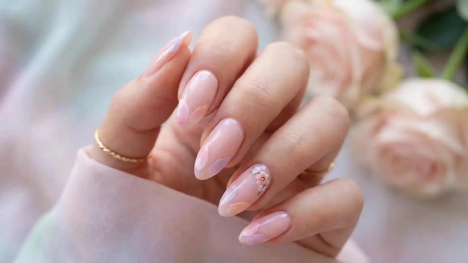 Hand with almond Petal Touch nails in soft pink, glossy finish with delicate floral nail art accents
