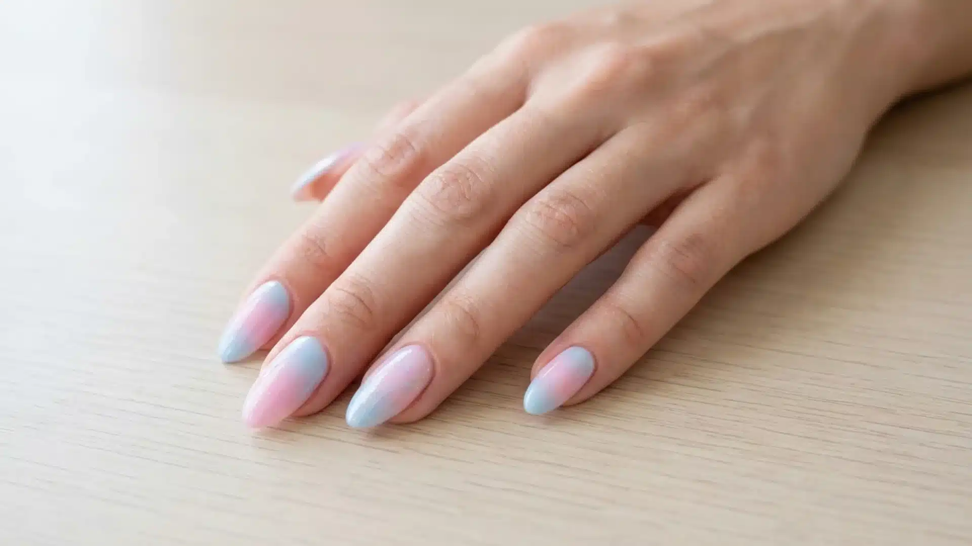 Hand with Cotton Candy nails in soft pink and baby blue ombre blend on glossy almond-shaped nails