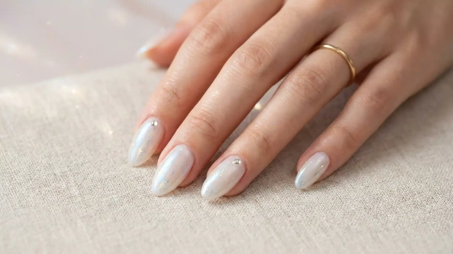 Hand with Crystal Veil nails featuring sheer milky shimmer polish with subtle glitter and tiny rhinestone