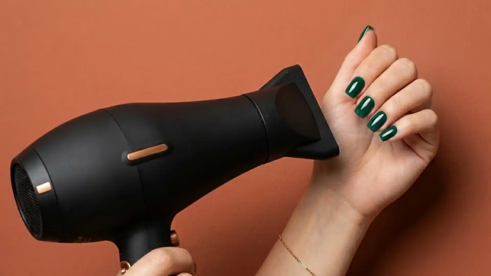 Hand with glossy green nails near a black hair dryer against a warm peach background for fast drying tips