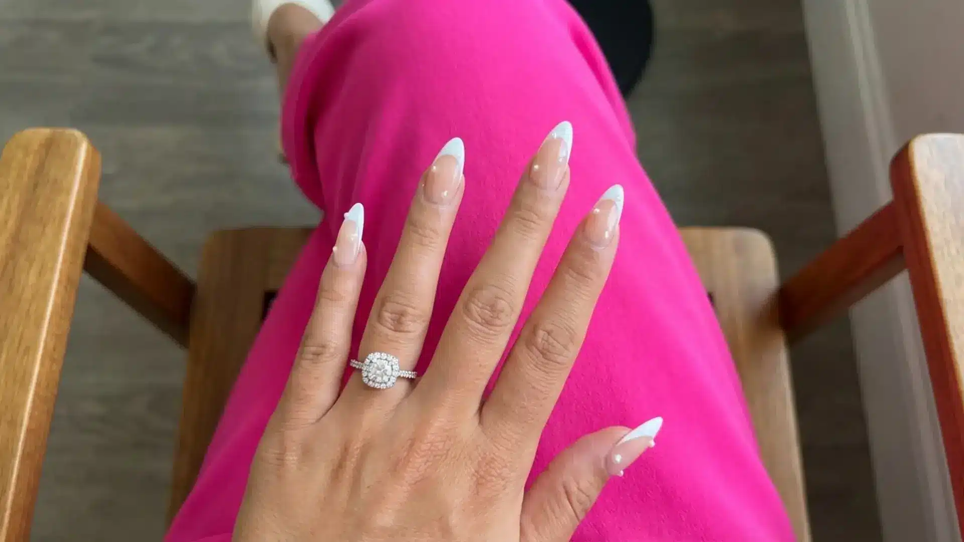 Hand with pearl accent bridesmaids nails and diamond ring resting on pink outfit