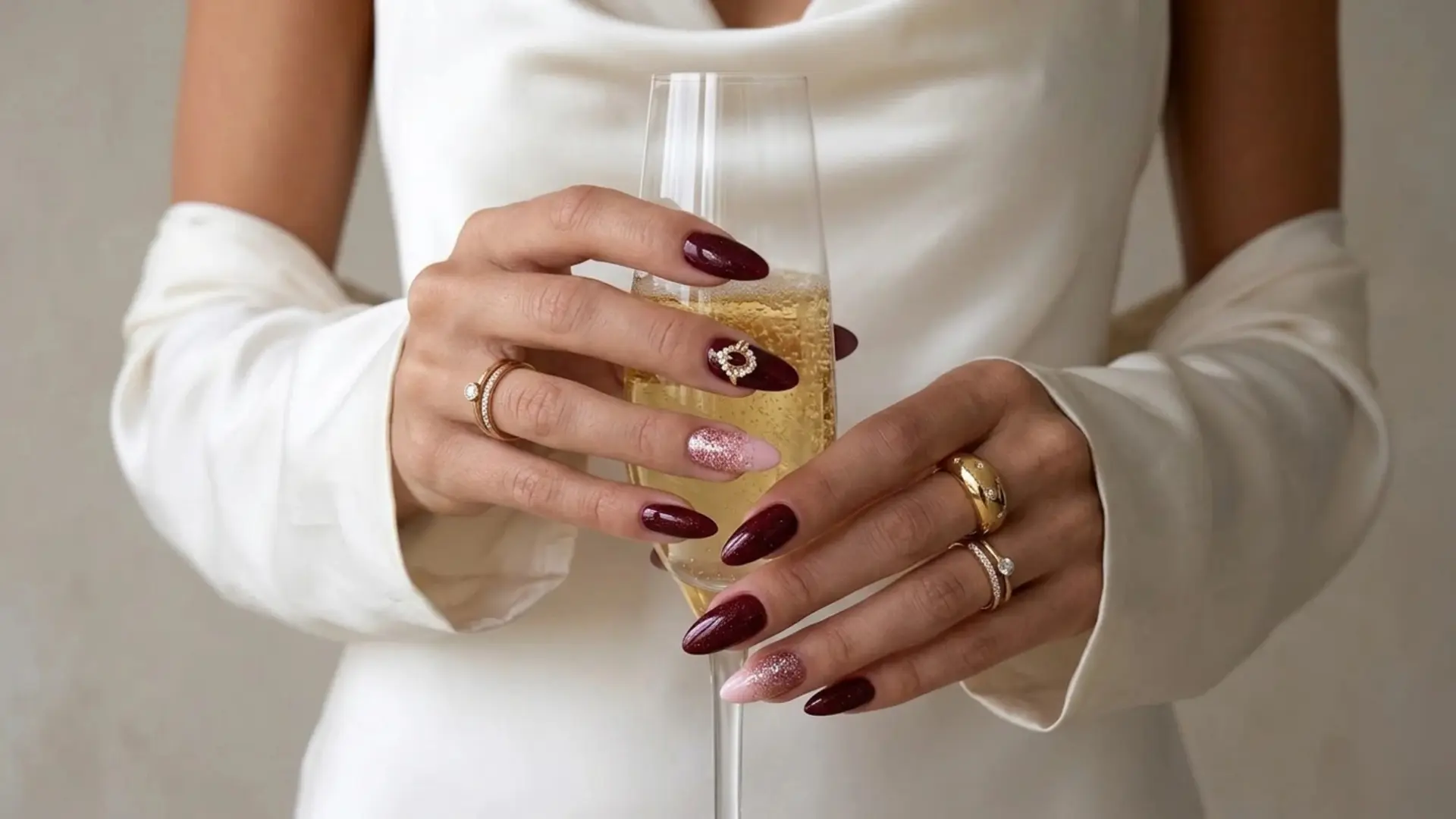 Hand holding champagne glass with burgundy almond nails with one glitter accent nail with shimmer