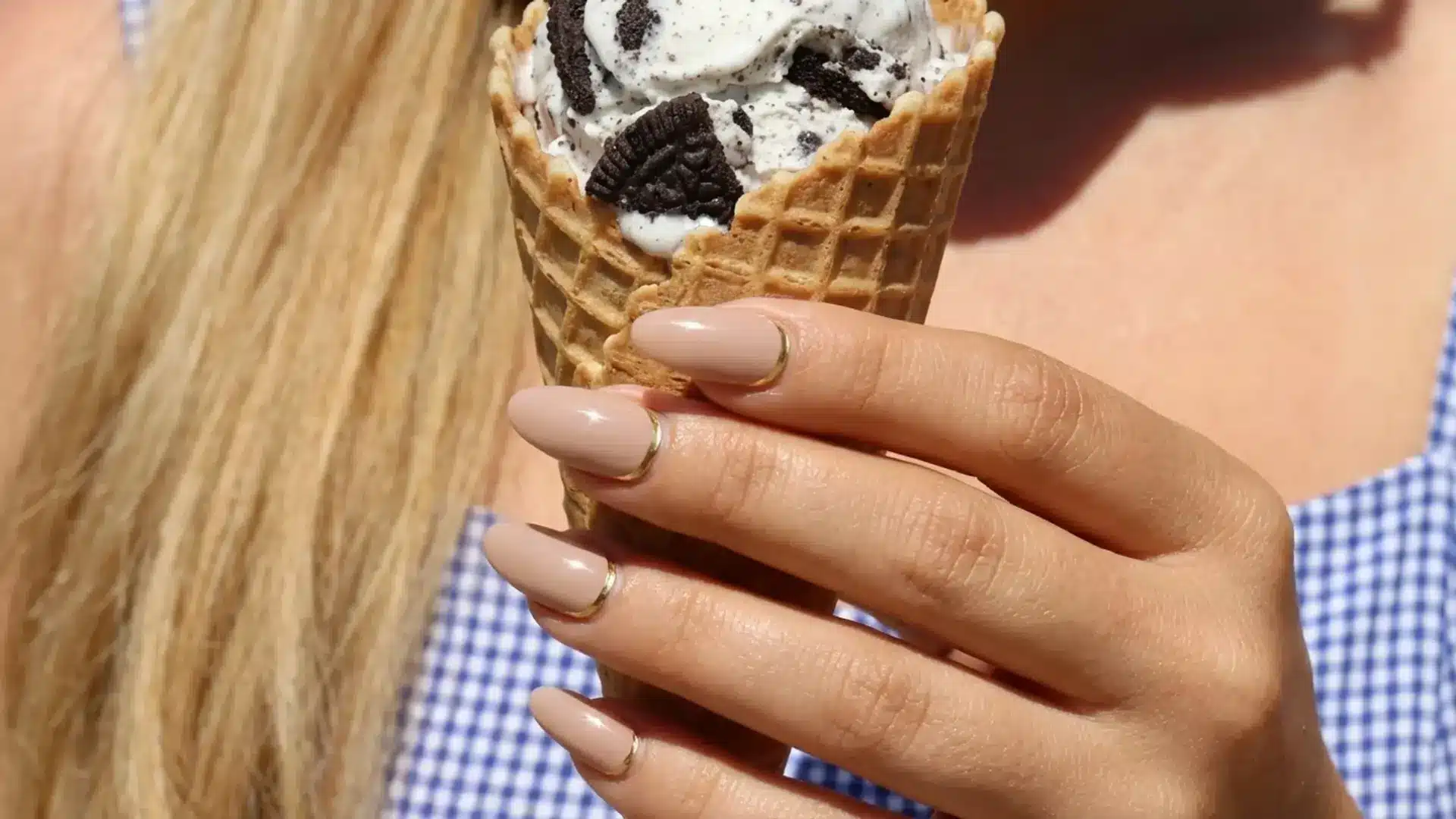 Hand holding ice cream cone with reverse French manicure featuring nude nails and thin gold outline near cuticle