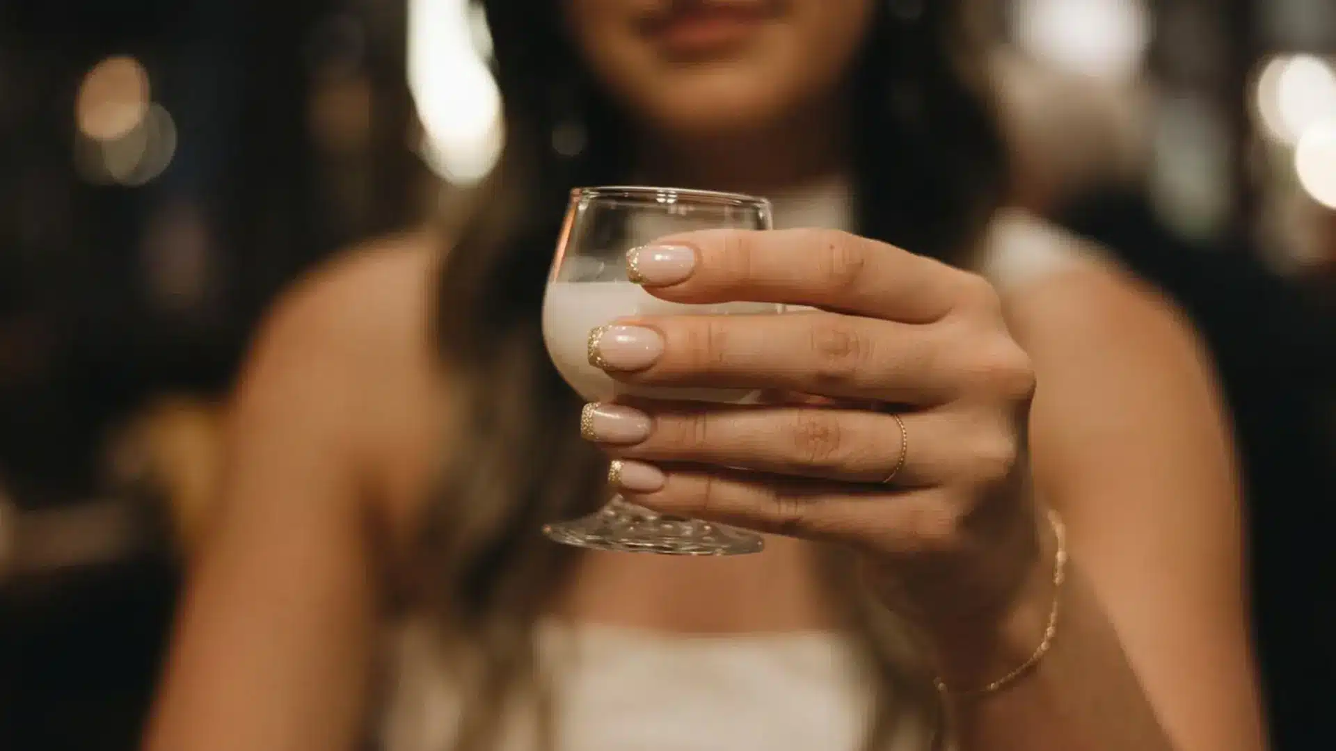 Hands with french tips with micro glitter edge manicure holding small glass showing party-ready bridemaid nail ideas