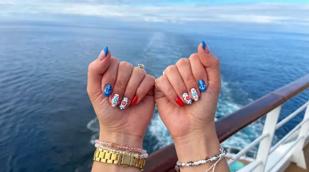 Hands with nautical themed nail art showing anchors hearts and stripes held over ocean view from cruise ship deck