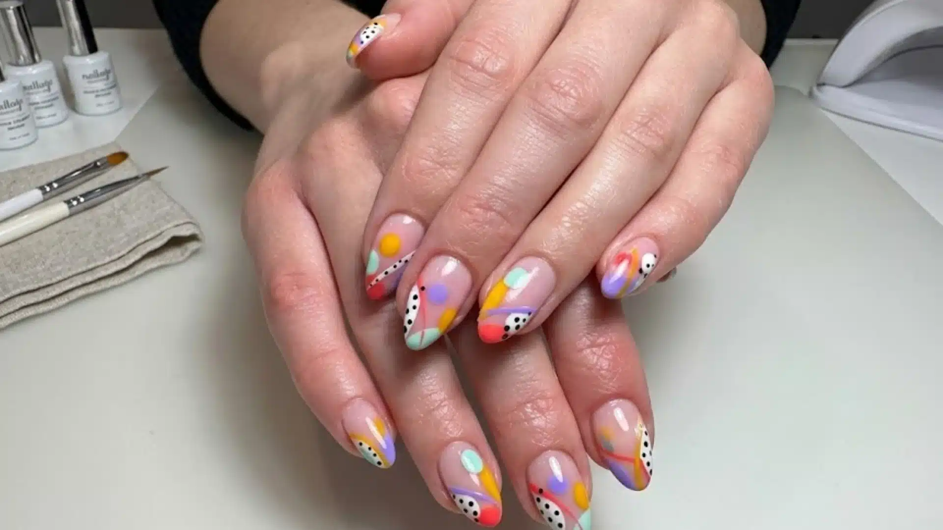 Hands with short oval nails featuring colorful abstract nail art, pastel shapes and dots, glossy finish