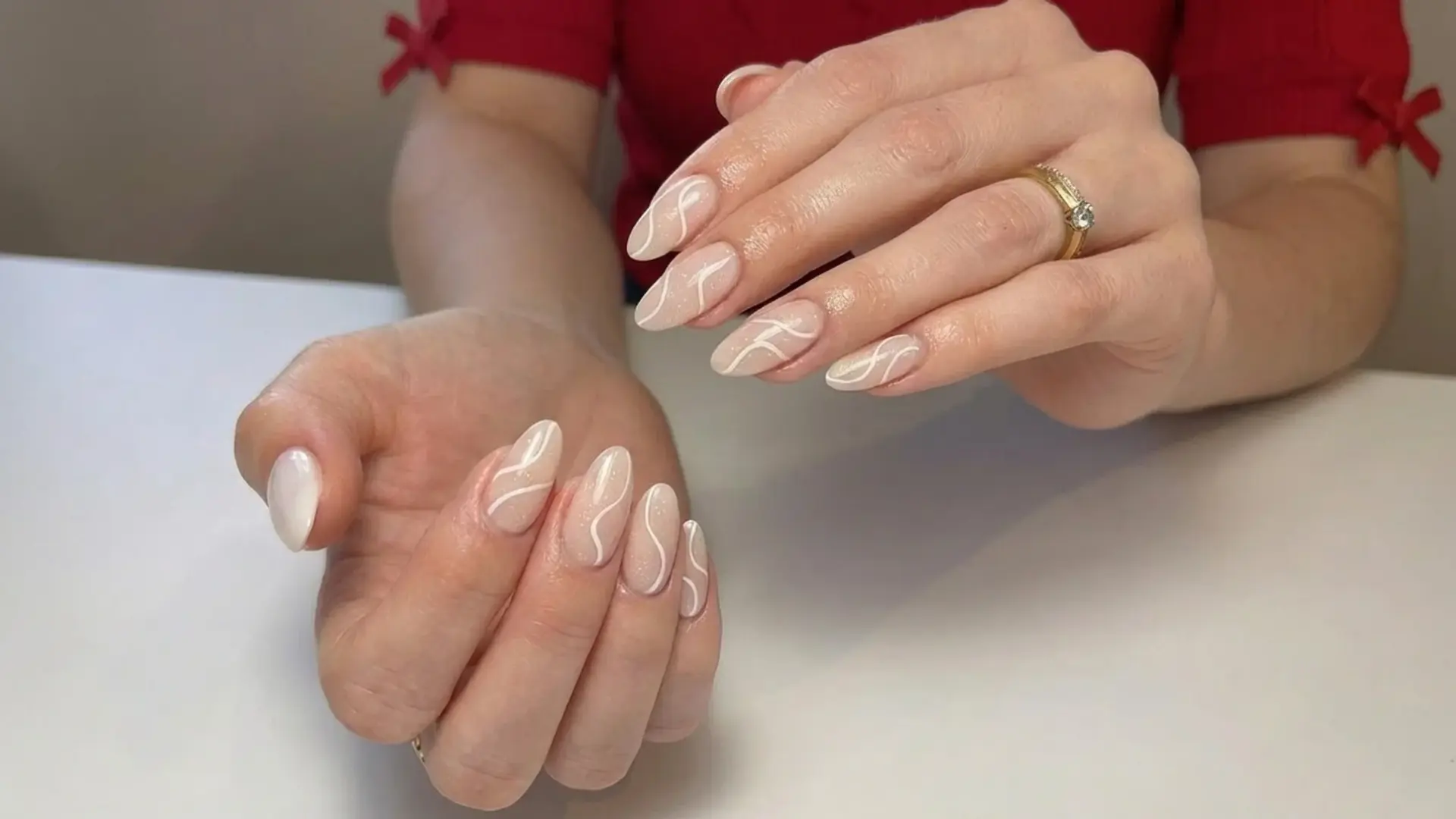 Hand showing negative space nails with sheer nude base and white abstract swirl lines on almond shaped nails