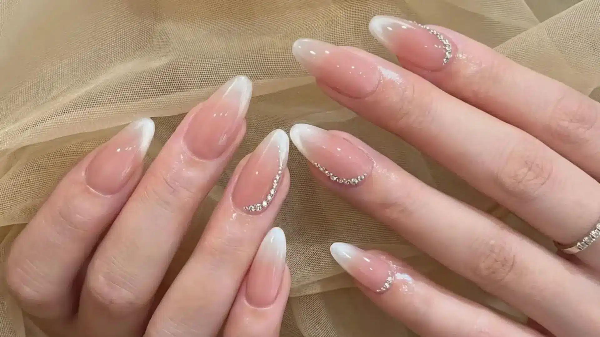 Hands with glossy mirror nails featuring sheer nude base and white tips with subtle shimmer and rhinestone detail