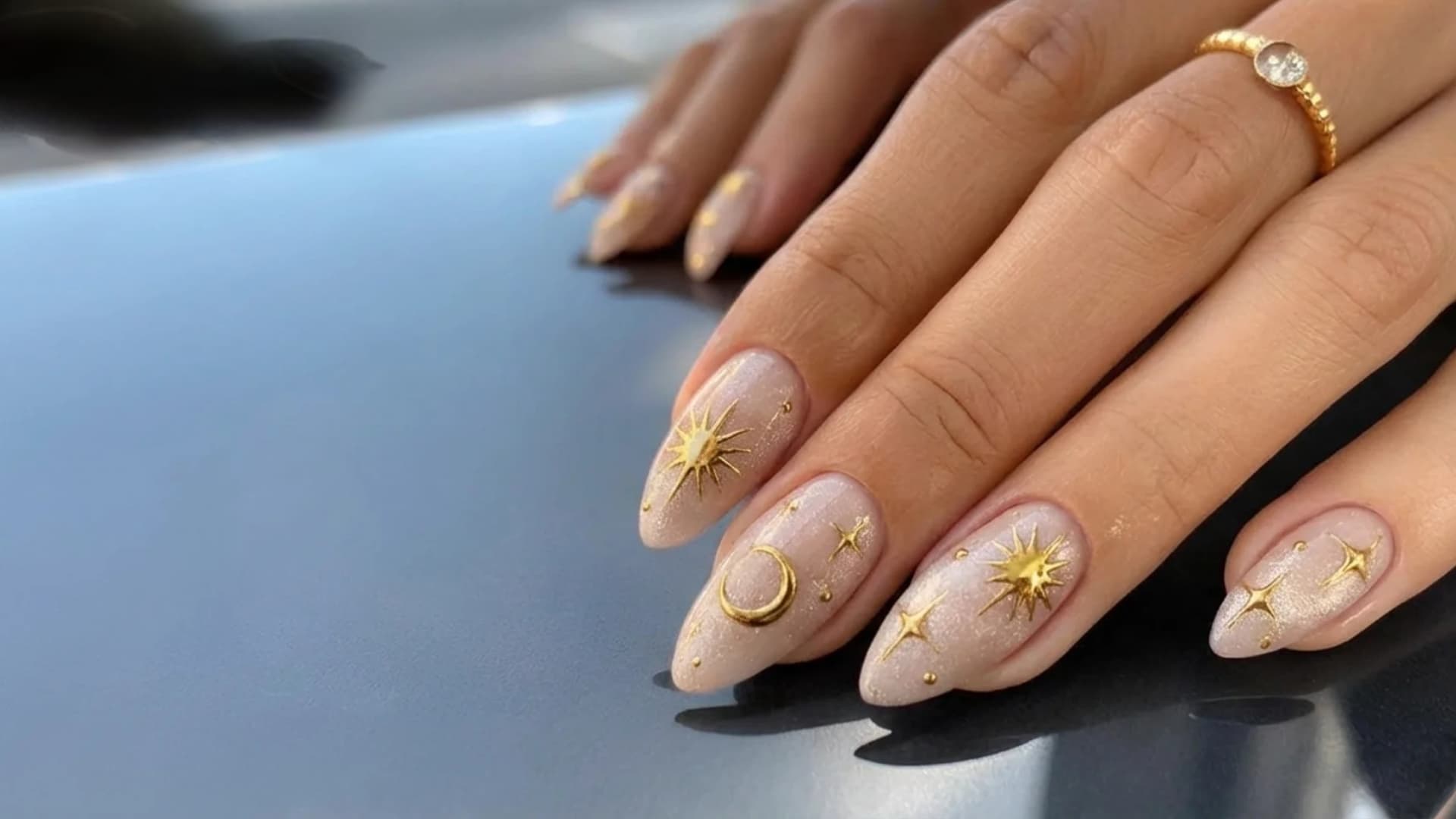 Hand with nude nails featuring gold celestial nail art with stars and moon details on almond shaped nails