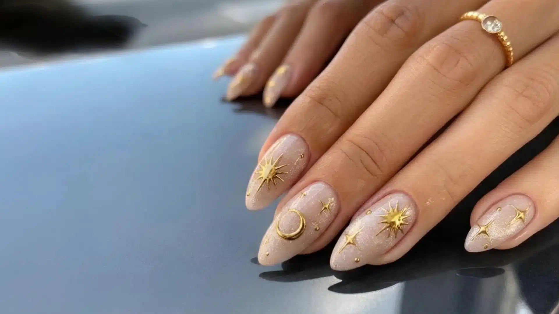 Hand with nude nails featuring gold celestial nail art with stars and moon details on almond shaped nails