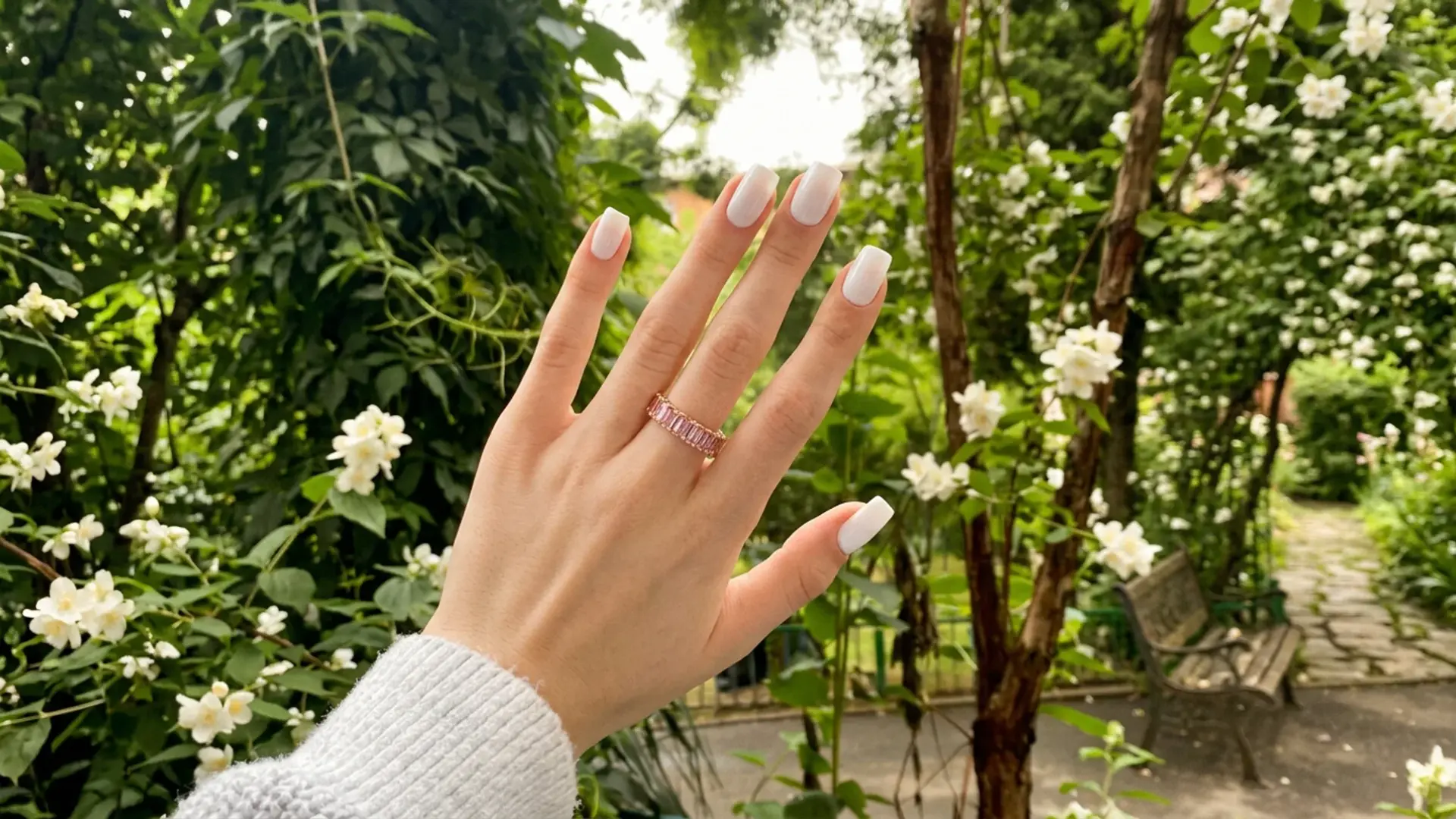Hand with short milk nails showing soft milky white polish on square shaped nails in outdoor garden setting
