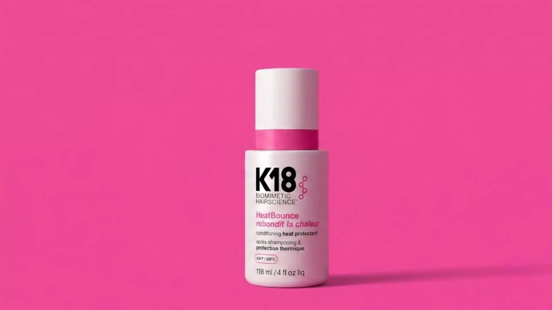 K18 HeatBounce conditioning heat protectant bottle on a bright pink background with soft studio lighting