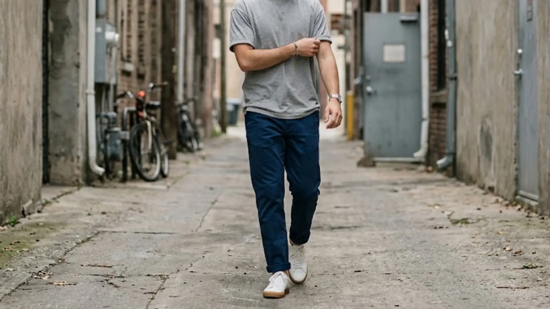 Man in gray t-shirt and blue chinos walking in urban alley with casual sneakers and relaxed style (1)