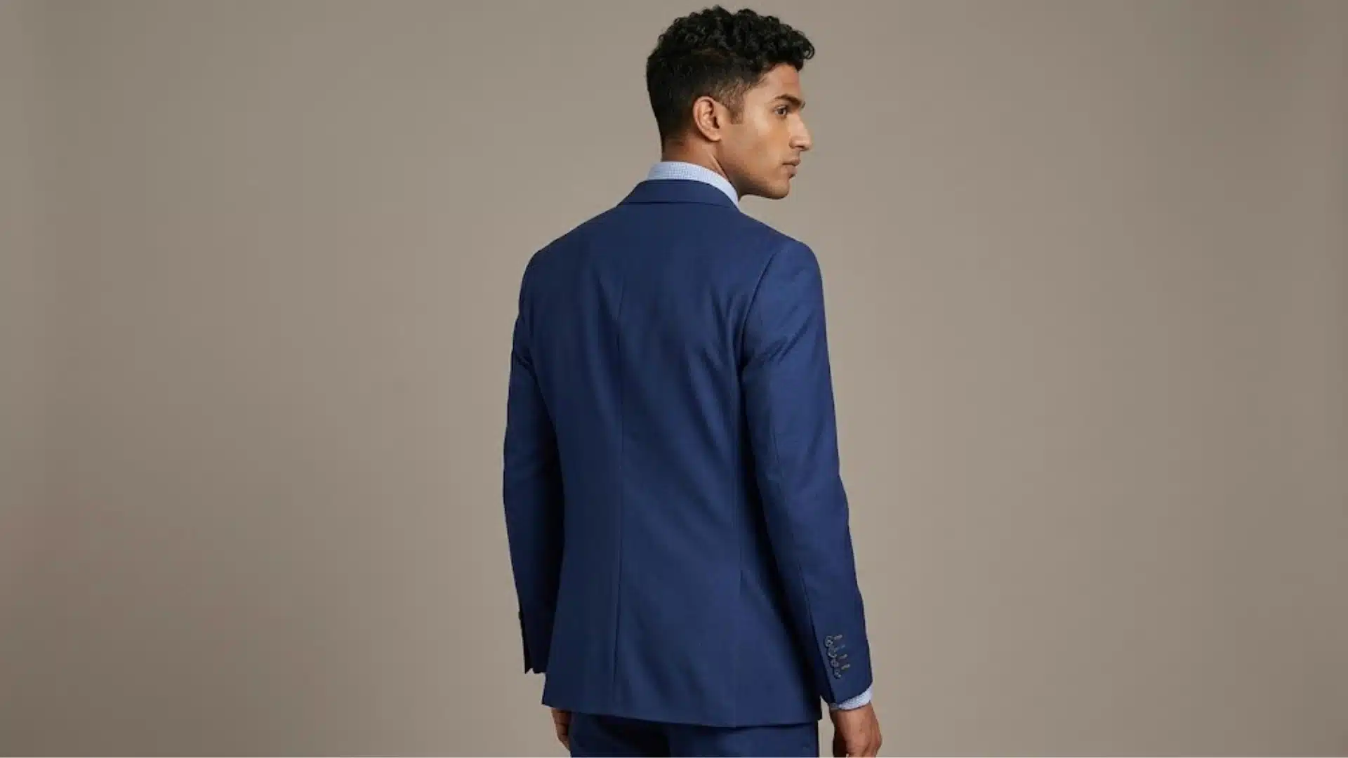 Man wearing a deep navy suit, shown from the back against a neutral background