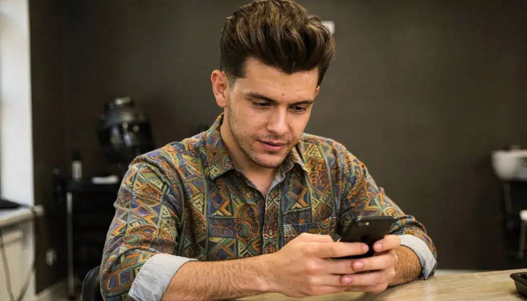 Man with a modern textured pompadour and tapered sides looking at his phone indoors