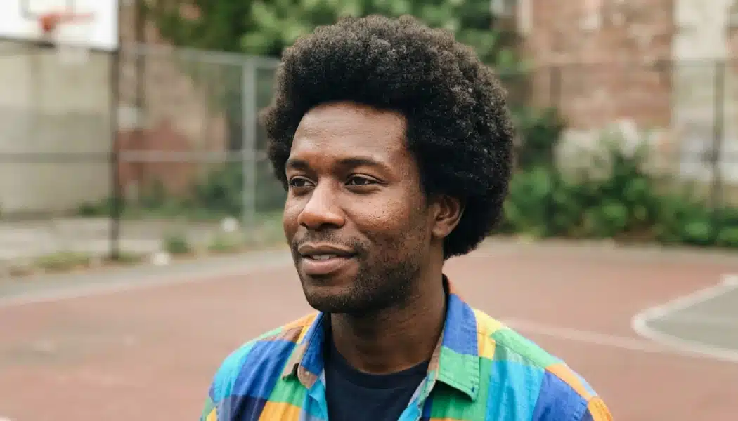 Man with a rounded afro and clean outline standing on an outdoor basketball court