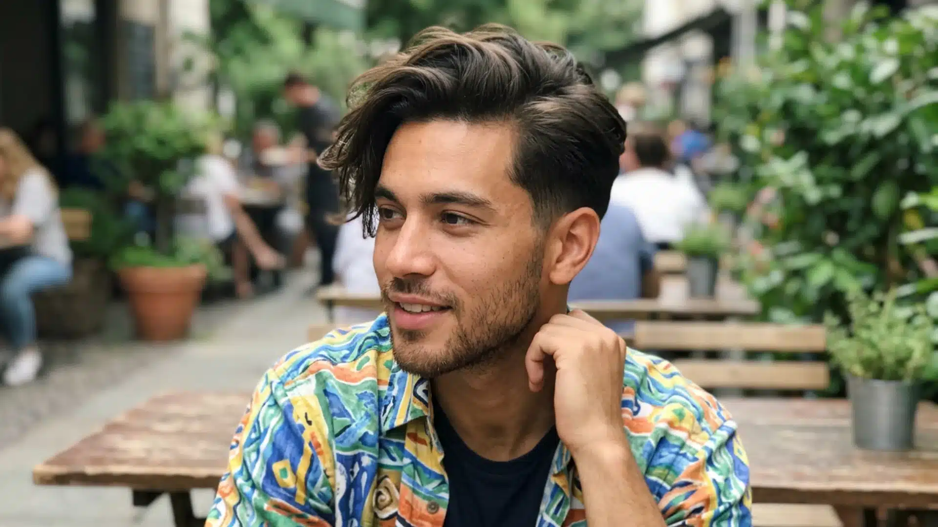 Man with a soft side sweep hairstyle, tapered sides, and colorful shirt at an outdoor cafe.