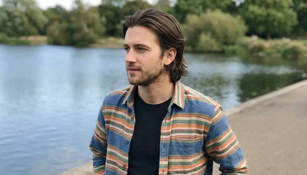 Man with bro flow hairstyle and pushed-back medium layers standing beside a lake