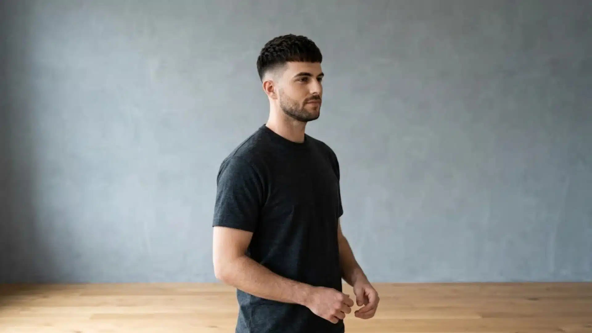 Man with French Crop haircut and short beard standing against a gray wall