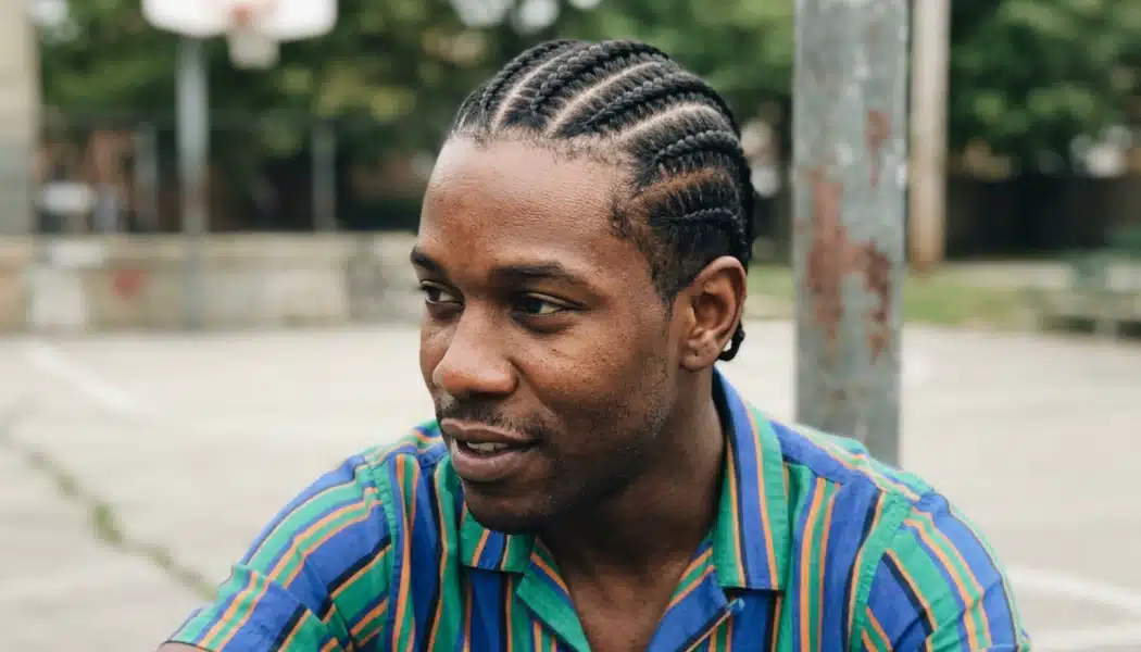 Man with neat cornrows and defined scalp partings sitting on an outdoor basketball court