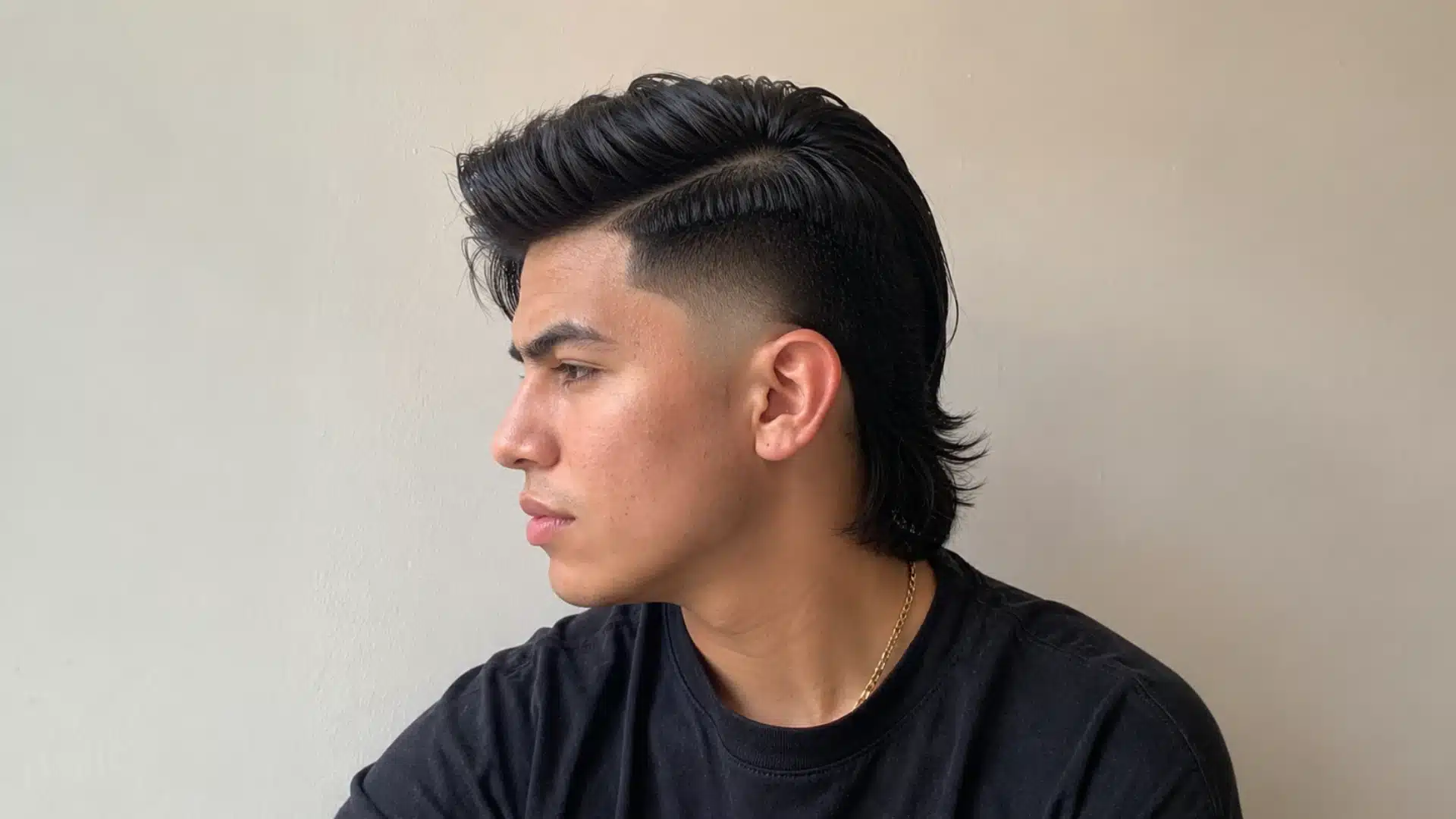Man with side part mullet fade, sharp faded sides, and brushed black hair against a plain wall