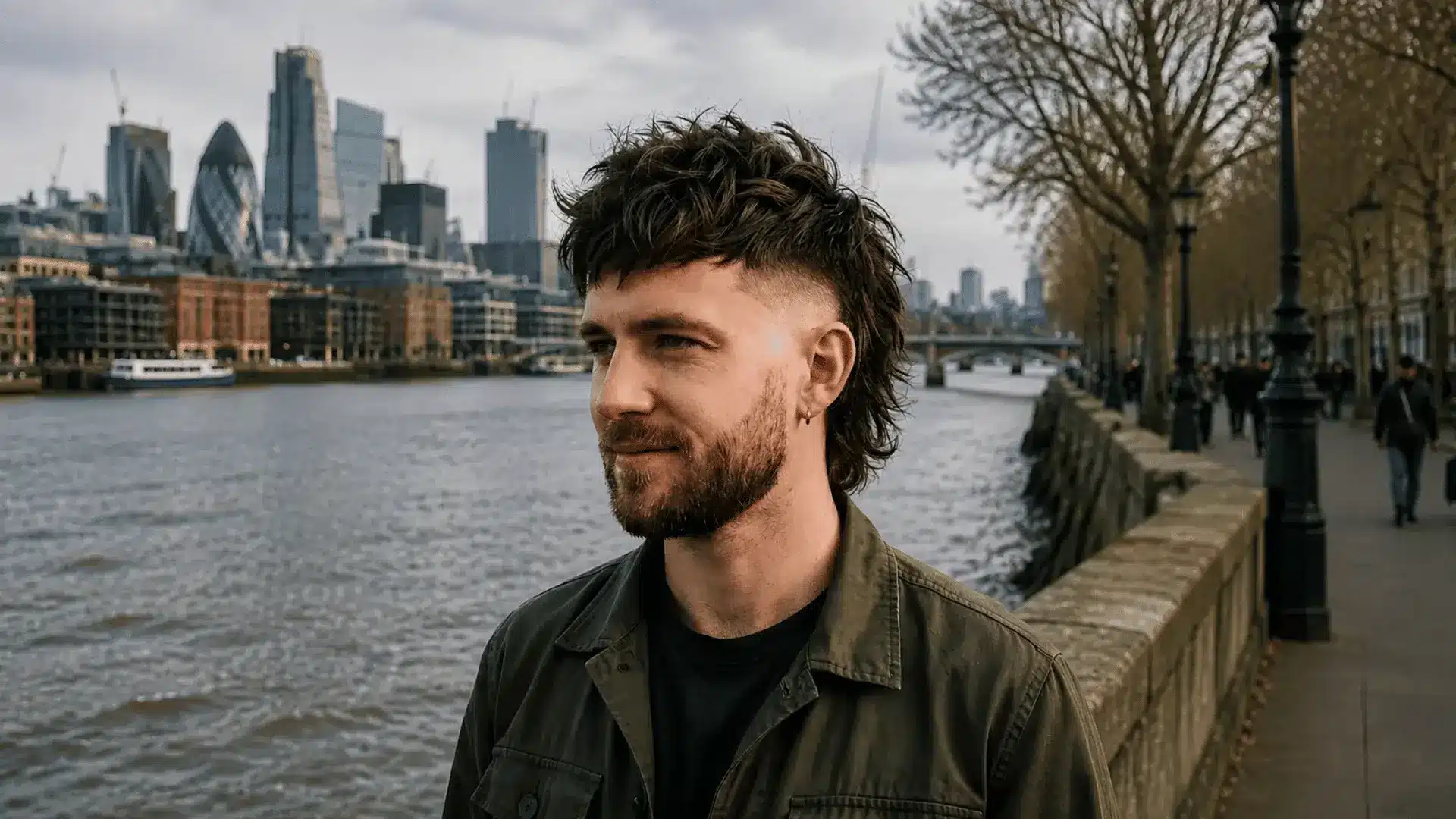 Man with textured fade mullet standing by a riverside promenade